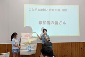 中学生がワークショップで使った付箋付きの模造紙を持って発表している写真